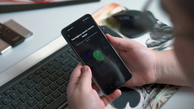 Main tenant un smartphone qui demande de poser le doigt sur le capteur d'empreinte, devant un clavier d'ordinateur